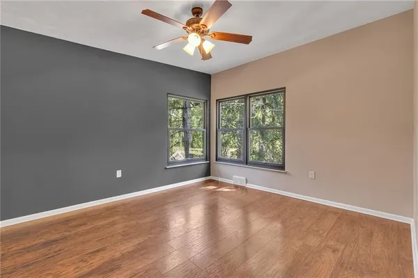 a view of an empty room with window a ceiling fan and wooden floor