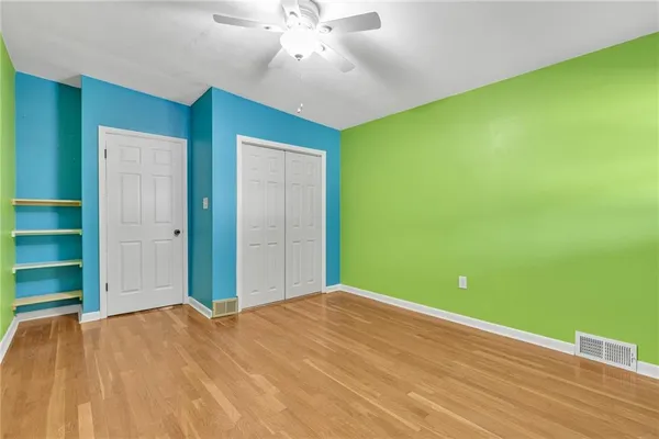 an empty room with wooden floor chandelier fan and windows