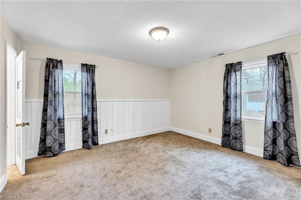 795 Dan Valley Road Madison, NC 27025 - Photo 23 of 38 Primary Bedroom: Features include carpet flooring to help keep your feet warm on cool mornings, a decorative chair rail to help protect the wall, wainscoting, 2 windows for natural lighting (the curtains stay with the home at closing) and fresh paint. The door on the left side is the primary bathroom.