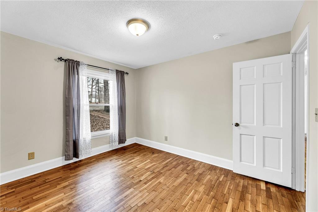 795 Dan Valley Road Madison, NC 27025 - Photo 25 of 38 Bedroom 2: Features include hardwood flooring for easy cleaning, a decorative chair rail to help protect the wall, wainscoting, a window for natural lighting and fresh paint. The door to the right side is the entry door.
