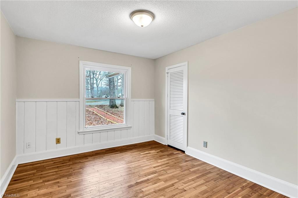 795 Dan Valley Road Madison, NC 27025 - Photo 26 of 38 Bedroom 3: Features include hardwood flooring for easy cleaning, a decorative chair rail to help protect the wall, wainscoting, a window for natural lighting and fresh paint. The closet is to the far right.