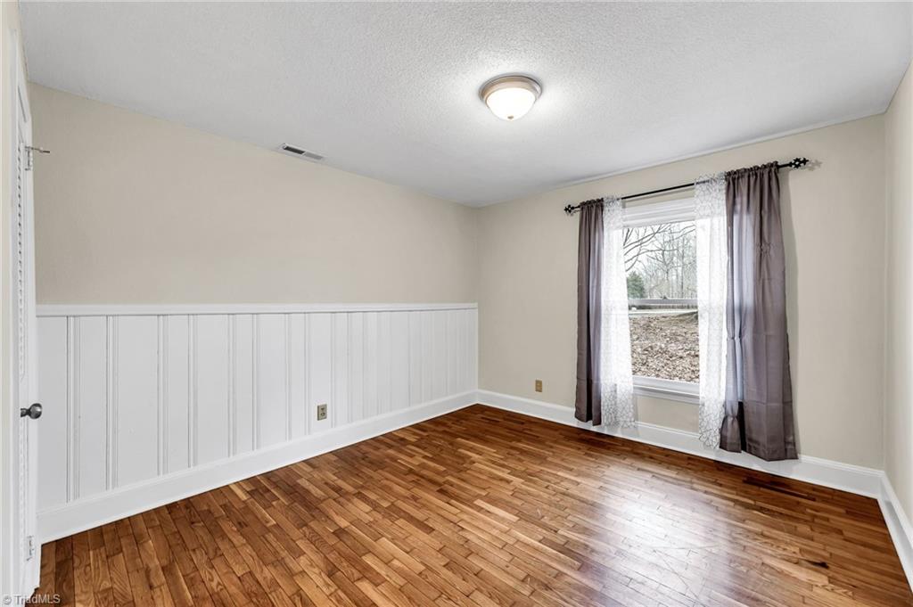 795 Dan Valley Road Madison, NC 27025 - Photo 7 of 38 Bedroom 2: Features include hardwood flooring for easy cleaning a, decorative chair rail to help protect the wall, wainscoting, a window for natural lighting and fresh paint.