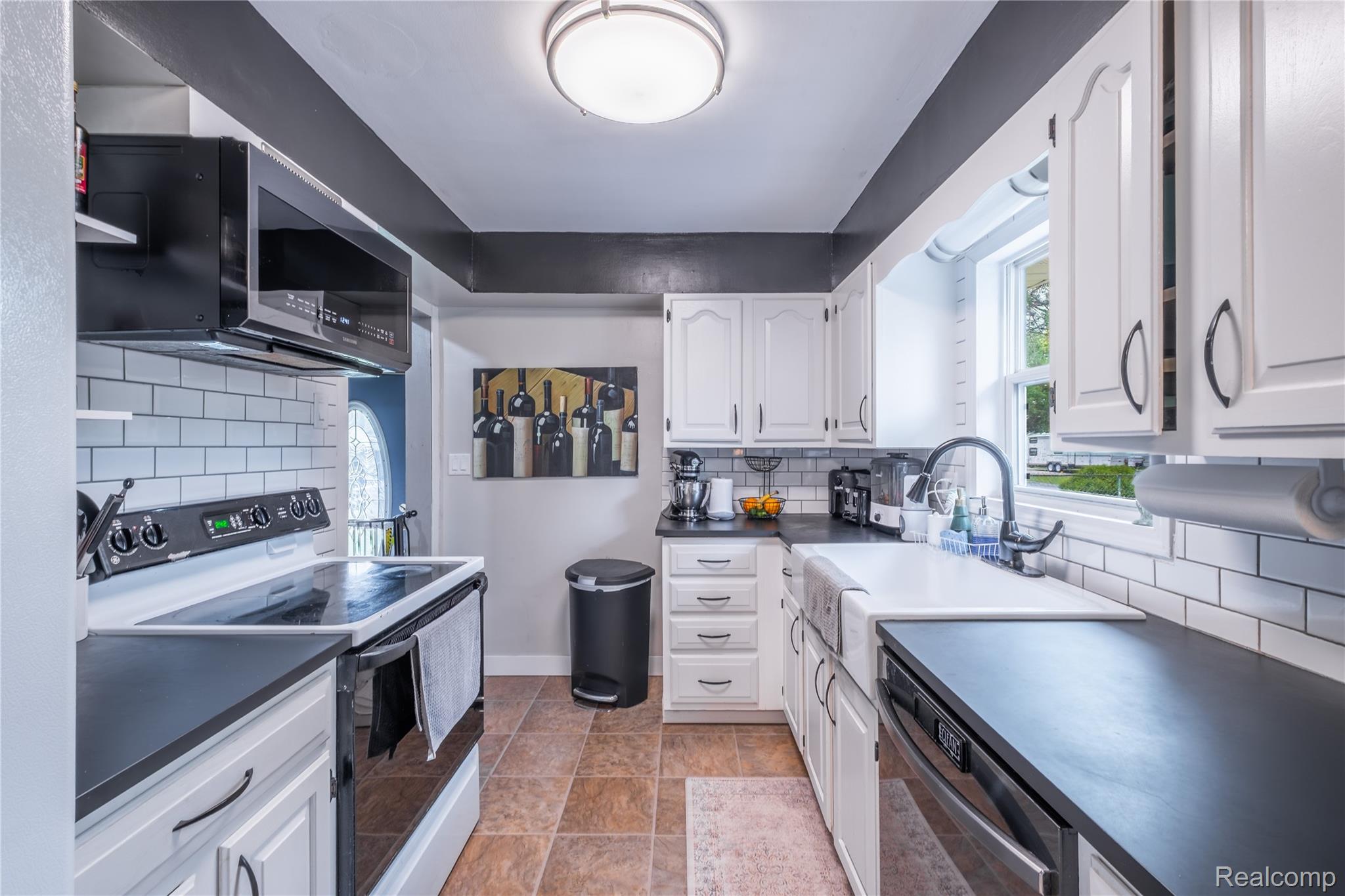 7800 Maple Street Birch Run, MI 48415 - Photo 7 of 29 Kitchen featuring white subway tile backsplash, white cabinetry with dark hardware, black countertops, and a white farmhouse sink with a black gooseneck faucet