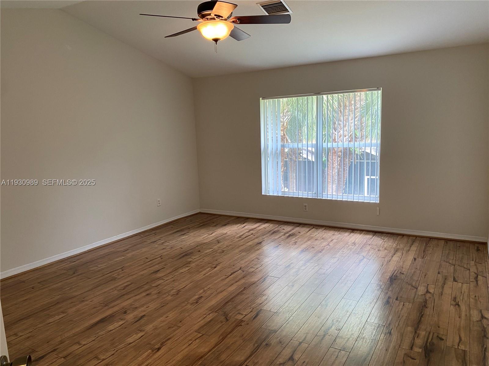 112 Wakulla Springs Way, Unit 112 Royal Palm Beach, FL 33411 - Photo 10 of 20 an empty room with wooden floor chandelier fan and windows