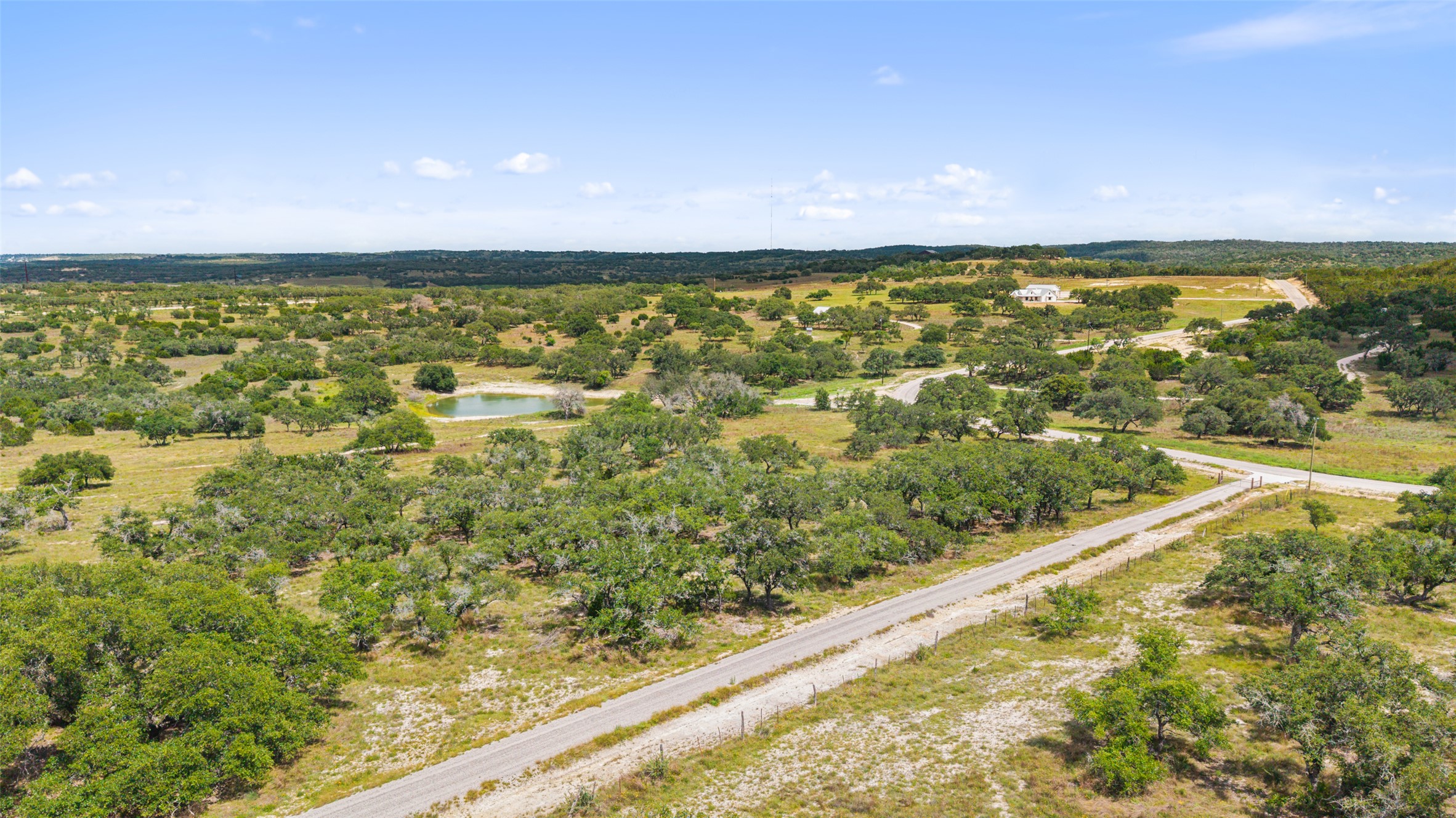 4112 Schumann Road Stonewall, TX 78671 - Photo 9 of 10 An aerial perspective reveals the property's vast acreage, featuring scattered trees, a natural pond, and winding country roads.
