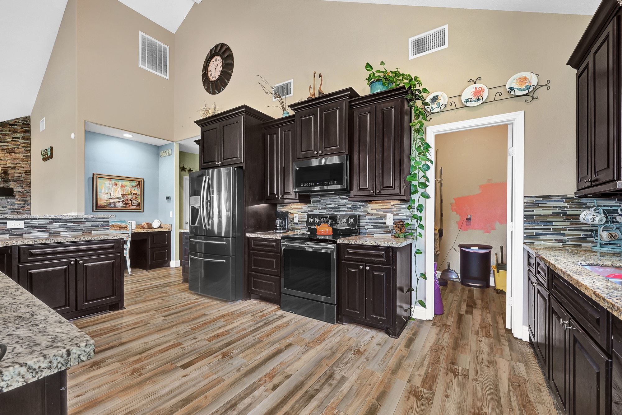 939 8th Street Dickinson, TX 77539 - Photo 13 of 31 This kitchen features dark wood cabinetry, granite countertops, and a stylish tile backsplash. It includes modern appliances, ample counter space, and an open layout. The adjacent room adds potential for customization. Perfect for a homebuyer who loves cooking and entertaining.
