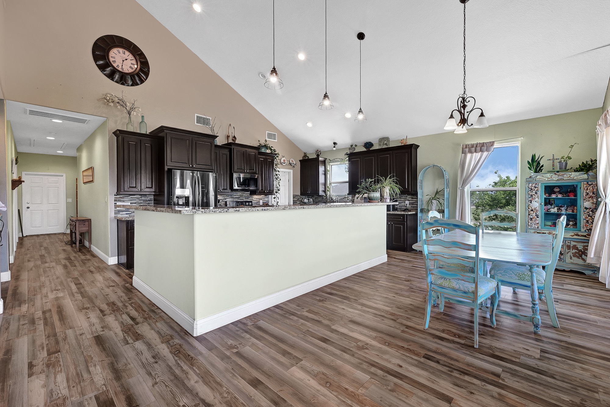 939 8th Street Dickinson, TX 77539 - Photo 14 of 31 This spacious kitchen features high ceilings, dark wood cabinets, and granite countertops. There's an open dining area with natural light from large windows, and stylish light fixtures add a modern touch. The hardwood floors and pastel accents create a warm, inviting atmosphere.