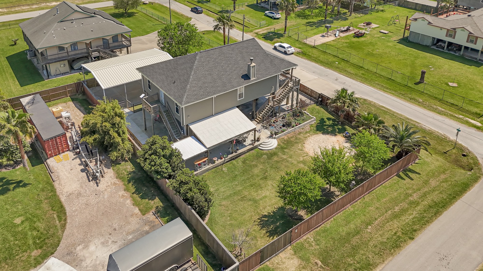 939 8th Street Dickinson, TX 77539 - Photo 20 of 31 This aerial view showcases a well-maintained two-story home with a spacious fenced yard. It features a covered porch and driveways, surrounded by lush greenery and situated on a quiet corner lot in a suburban neighborhood.