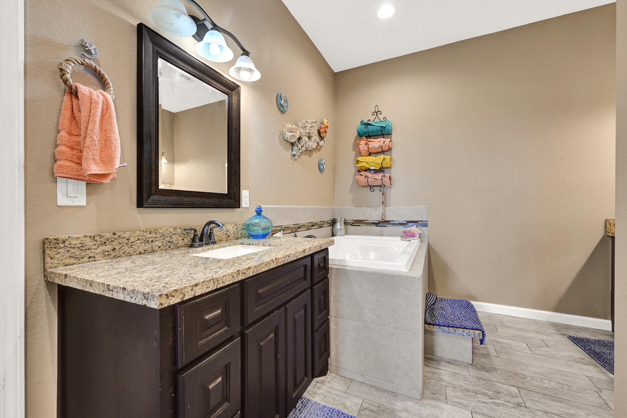 939 8th Street Dickinson, TX 77539 - Photo 25 of 31 This bathroom features a granite countertop with a dark wood vanity, a large mirror, and recessed lighting. It has a soaking tub with tiled surround and neutral wall colors, creating a cozy and stylish space.