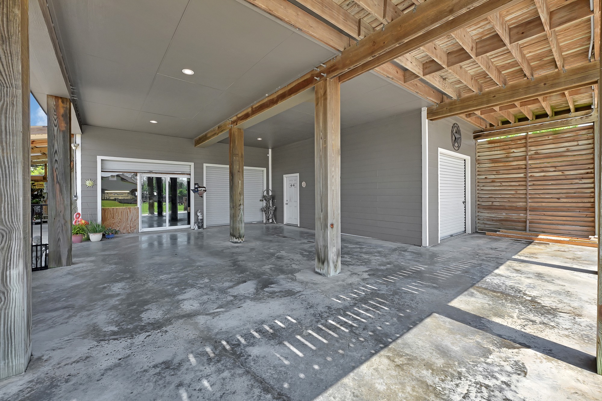 939 8th Street Dickinson, TX 77539 - Photo 7 of 31 This photo showcases a spacious, covered outdoor area with concrete flooring and wooden beams. It features sliding glass doors, storage space with roll-up doors, and ample room for parking or outdoor activities.