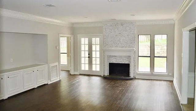 an empty room with wooden floor fireplace and windows
