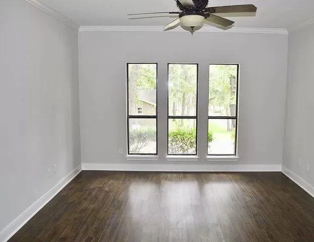 an empty room with wooden floor fan and windows