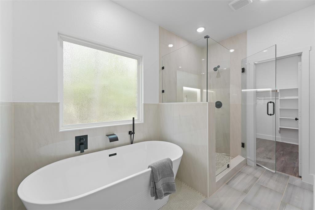 122 East Beachwood Loop Trinidad, TX 75163 - Photo 22 of 35 Contemporary bathroom featuring a freestanding soaking tub with matte black fixtures, a spacious glass-enclosed shower with tiled walls and pebble flooring, and large format floor tiling