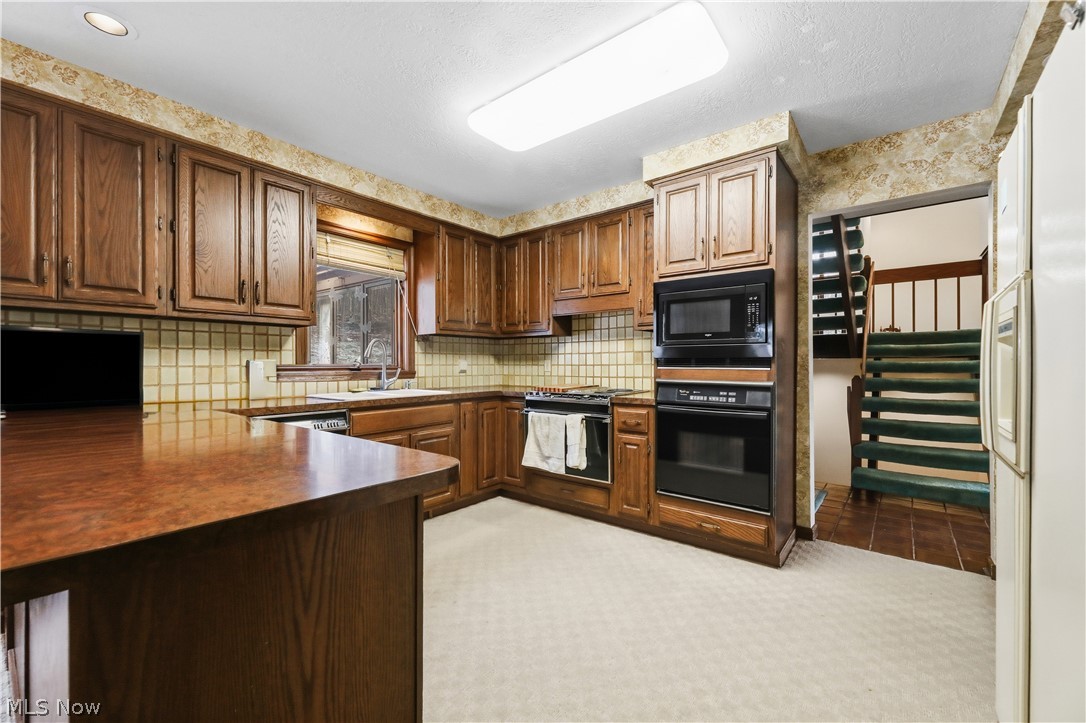 7014 River Styx Road Medina, OH 44256 - Photo 12 of 50 Kitchen with black appliances, dark countertops, a peninsula, wallpapered walls, and brown cabinets
