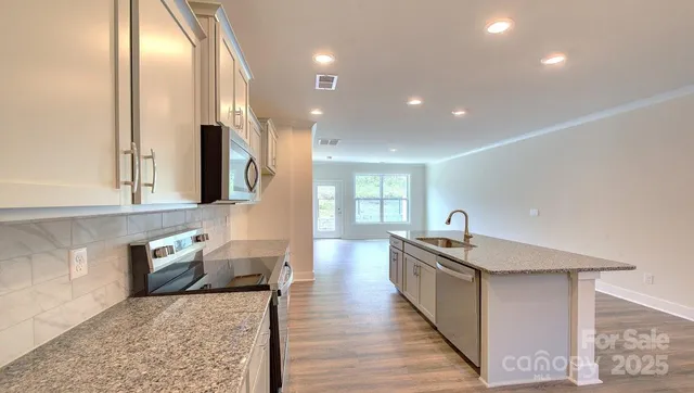 a kitchen with stainless steel appliances granite countertop a sink a stove and a wooden floors