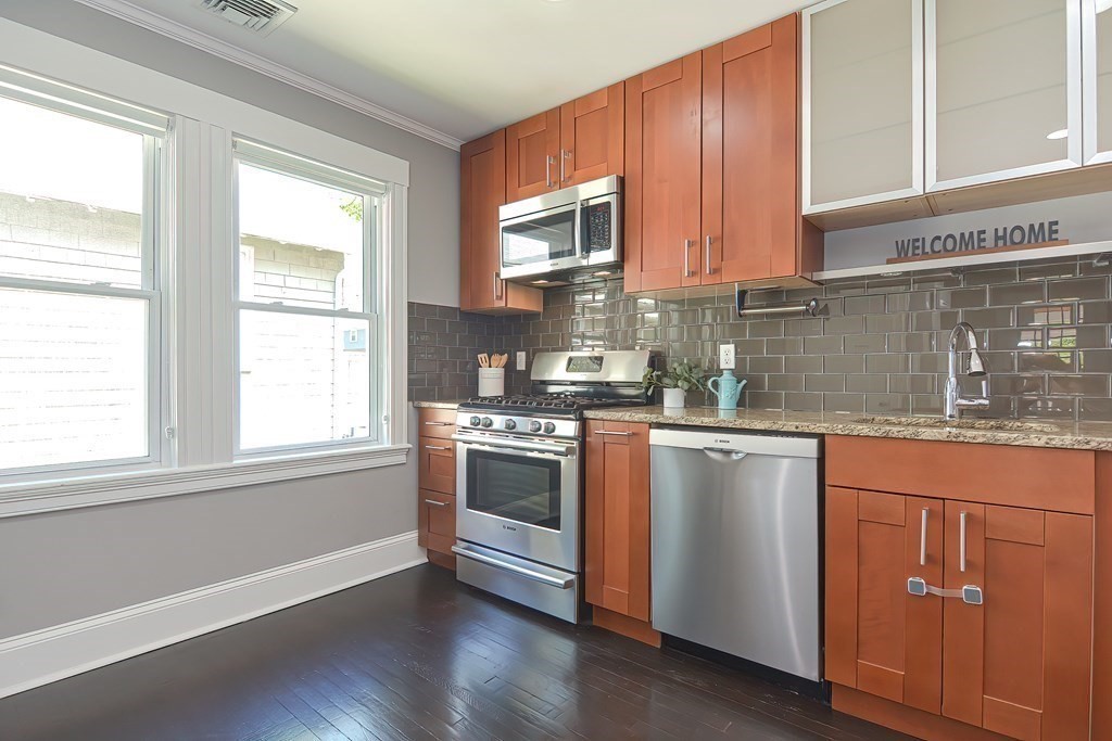7-9 Goodway Road, Unit 2 Jamaica Plain, MA 02130 - Photo 11 of 39 a kitchen with granite countertop wooden cabinets stainless steel appliances a sink and a window