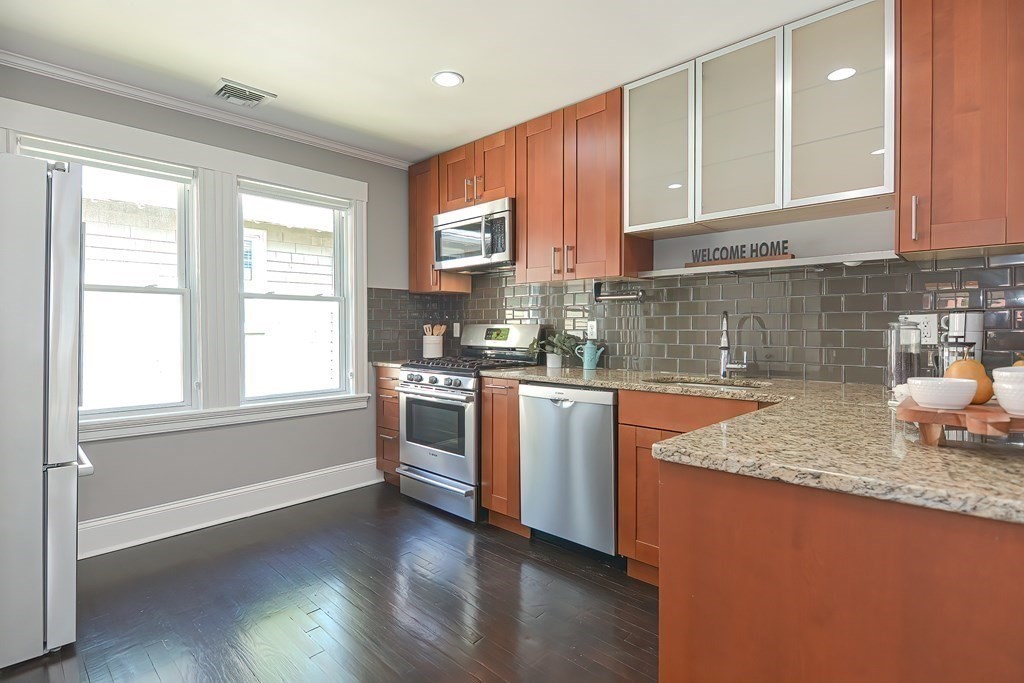 7-9 Goodway Road, Unit 2 Jamaica Plain, MA 02130 - Photo 13 of 39 a kitchen with granite countertop wooden cabinets a stove a sink and dishwasher with wooden floor