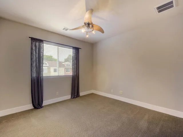 an empty room with chandelier fan and windows
