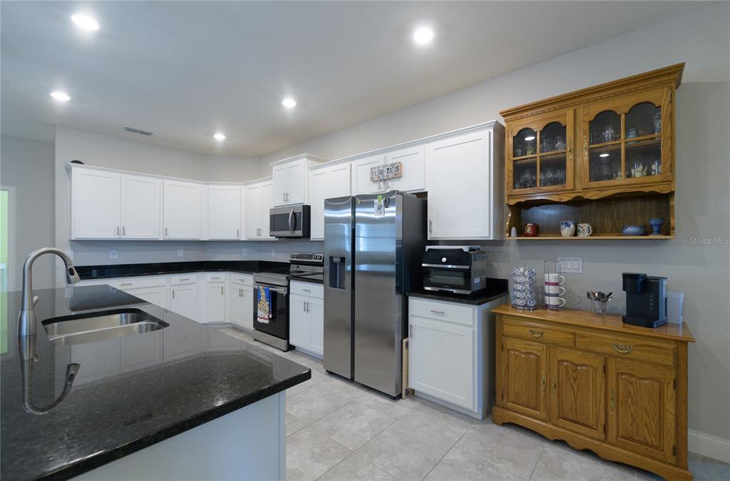 4444 Devinshire Fields Loop Plant City, FL 33567 - Photo 11 of 38 a kitchen with stainless steel appliances granite countertop a refrigerator a stove and a sink with wooden cabinets