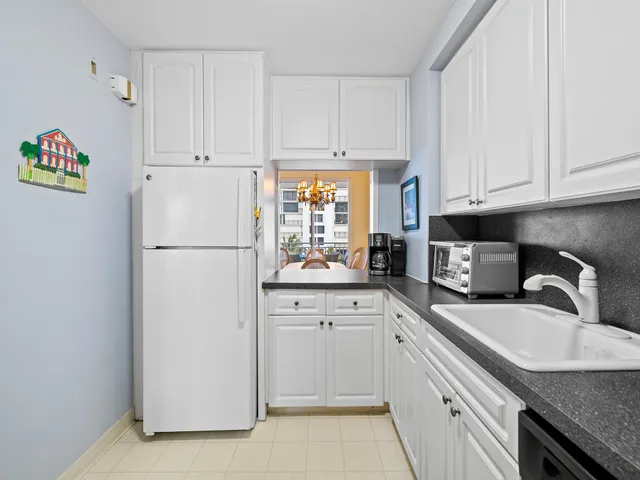 a kitchen with granite countertop a refrigerator a sink a stove and white cabinets
