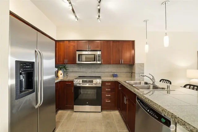 a kitchen with stainless steel appliances granite countertop a refrigerator a stove and a sink with wooden floor
