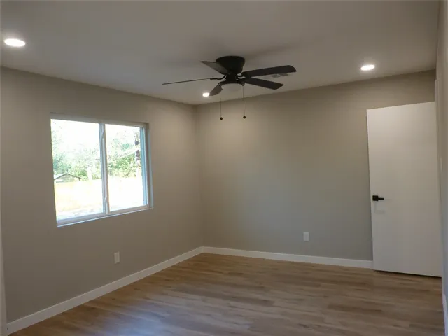 an empty room with wooden floor fan and windows