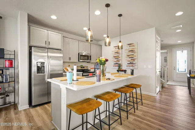 a kitchen with stainless steel appliances kitchen island granite countertop a refrigerator a stove top oven a sink dishwasher and white cabinets with wooden floor