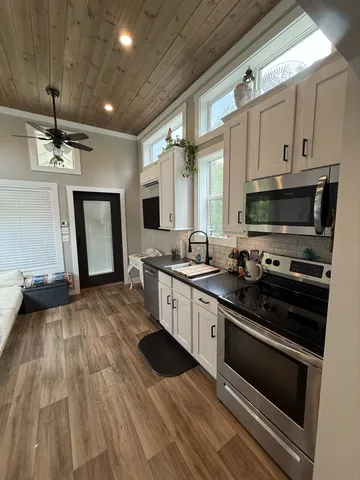 a kitchen with granite countertop a refrigerator a sink dishwasher a stove and white cabinets with wooden floor