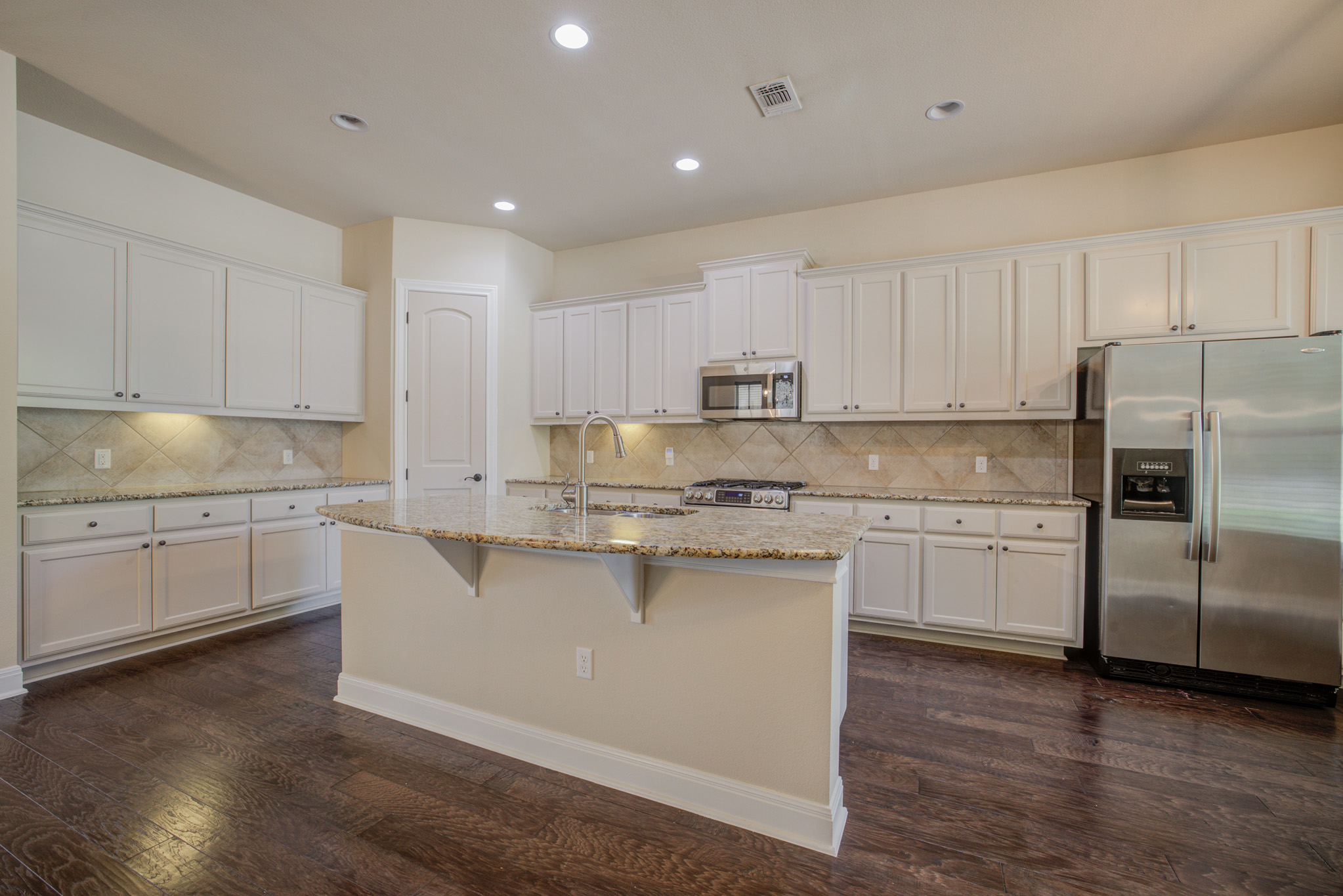 4524 Berkman Drive Austin, TX 78723 - Photo 7 of 38 Contemporary kitchen featuring an island with a sink and breakfast bar, white cabinetry, granite countertops, stainless steel appliances, and wood-finish flooring
