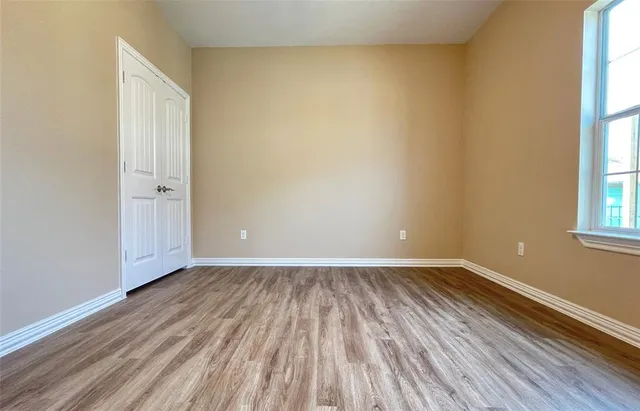 a view of an empty room with wooden floor and a window