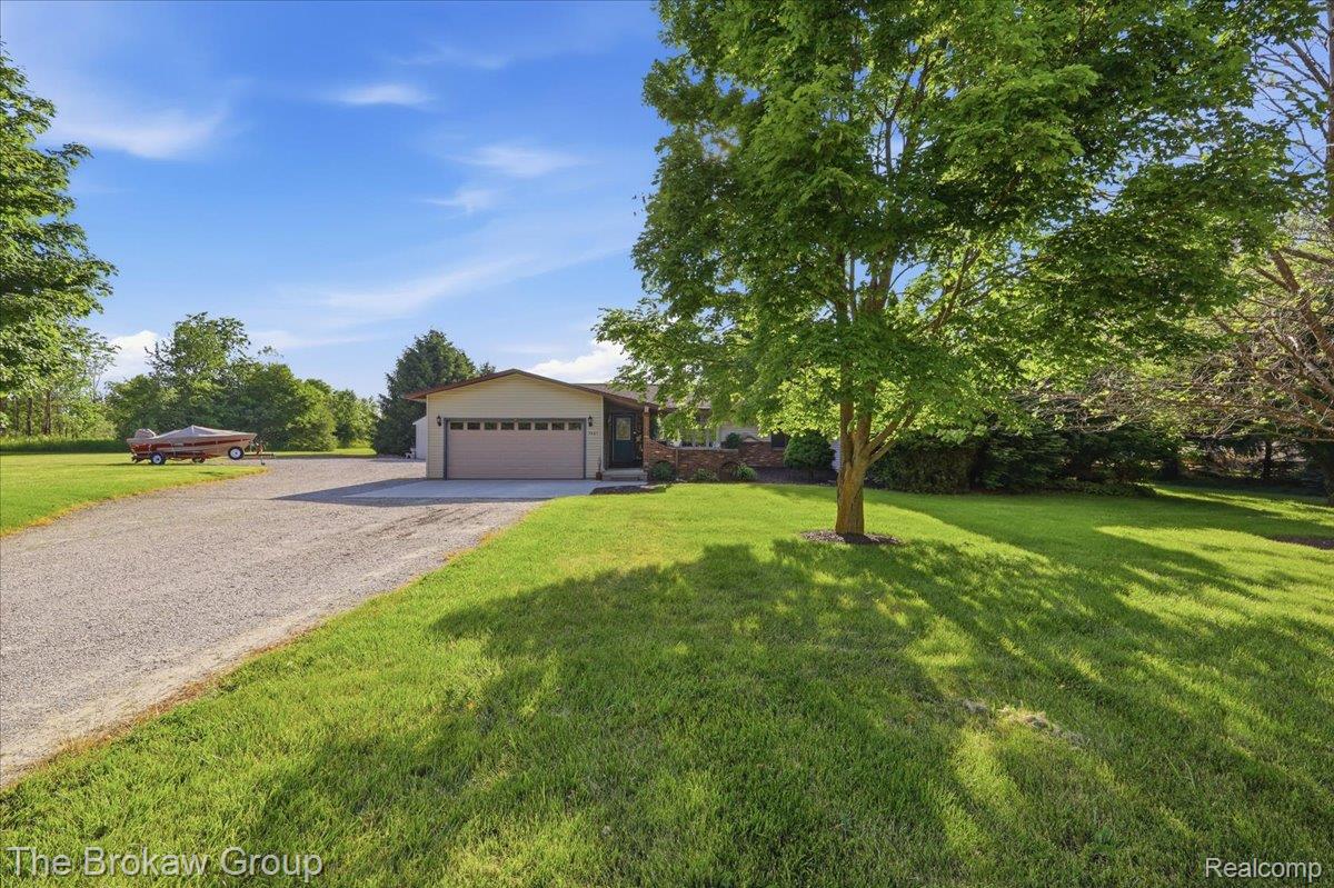 Expansive green lawn with mature trees and a gravel driveway leading to a two-car garage