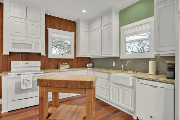 a kitchen with stainless steel appliances granite countertop a stove a sink dishwasher and white cabinets with wooden floor