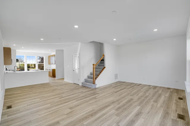 a view of an empty room with wooden floor and a kitchen