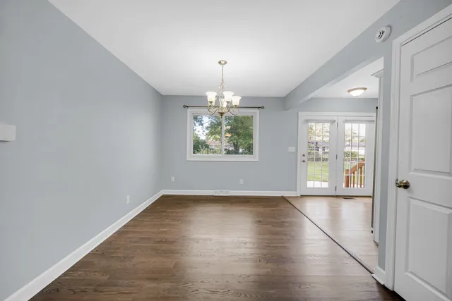 an empty room with wooden floor chandelier and windows