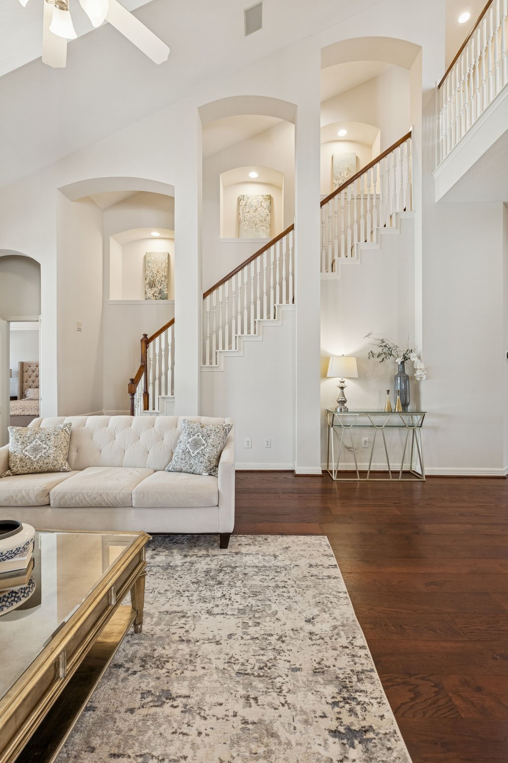 2202 Britton Ridge Drive Katy, TX 77494 - Photo 20 of 41 Dramatic two-story living space showcasing soaring ceilings, elegant architectural niches, and rich wood flooring, with the staircase leading exclusively to the upstairs versatile space for a game room, billiards lounge, or anything you can imagine —perfectly designed for entertaining while keeping the rest of the home conveniently on one level.