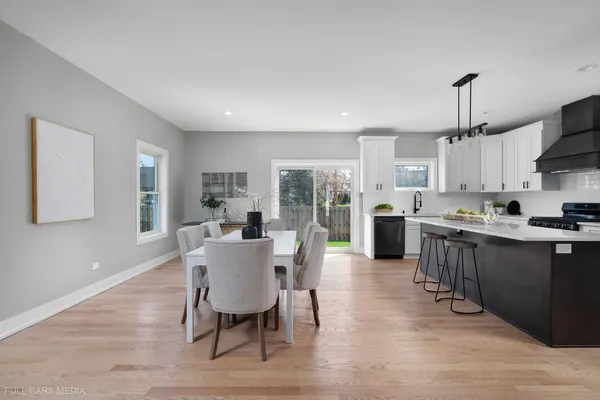 a large white kitchen with stainless steel appliances granite countertop a stove a sink dishwasher a dining table and chairs with wooden floor