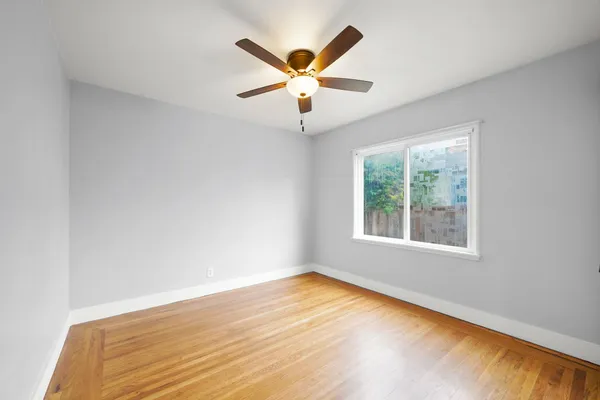 a view of an empty room with wooden floor and a ceiling fan