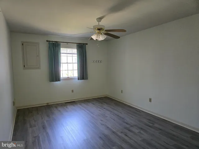 an empty room with wooden floor windows and fan
