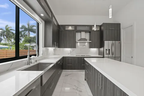 a large kitchen with a large counter top a sink a counter top space stainless steel appliances a large window and cabinets