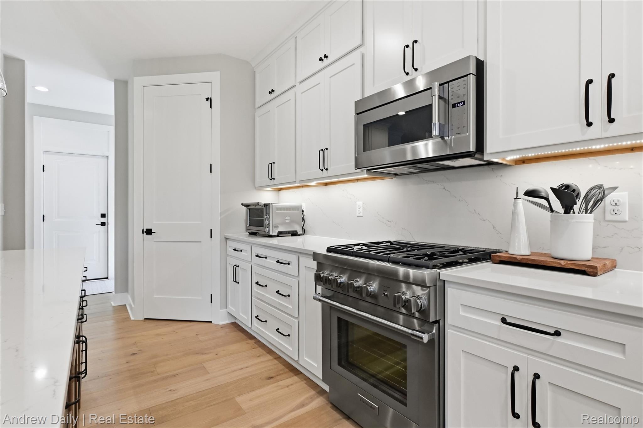 4661 Spears Road Pinckney, MI 48169 - Photo 22 of 56 Modern kitchen featuring white shaker cabinetry with matte black hardware, stainless steel gas range with a matching microwave, white stone countertops, and wood-finish flooring