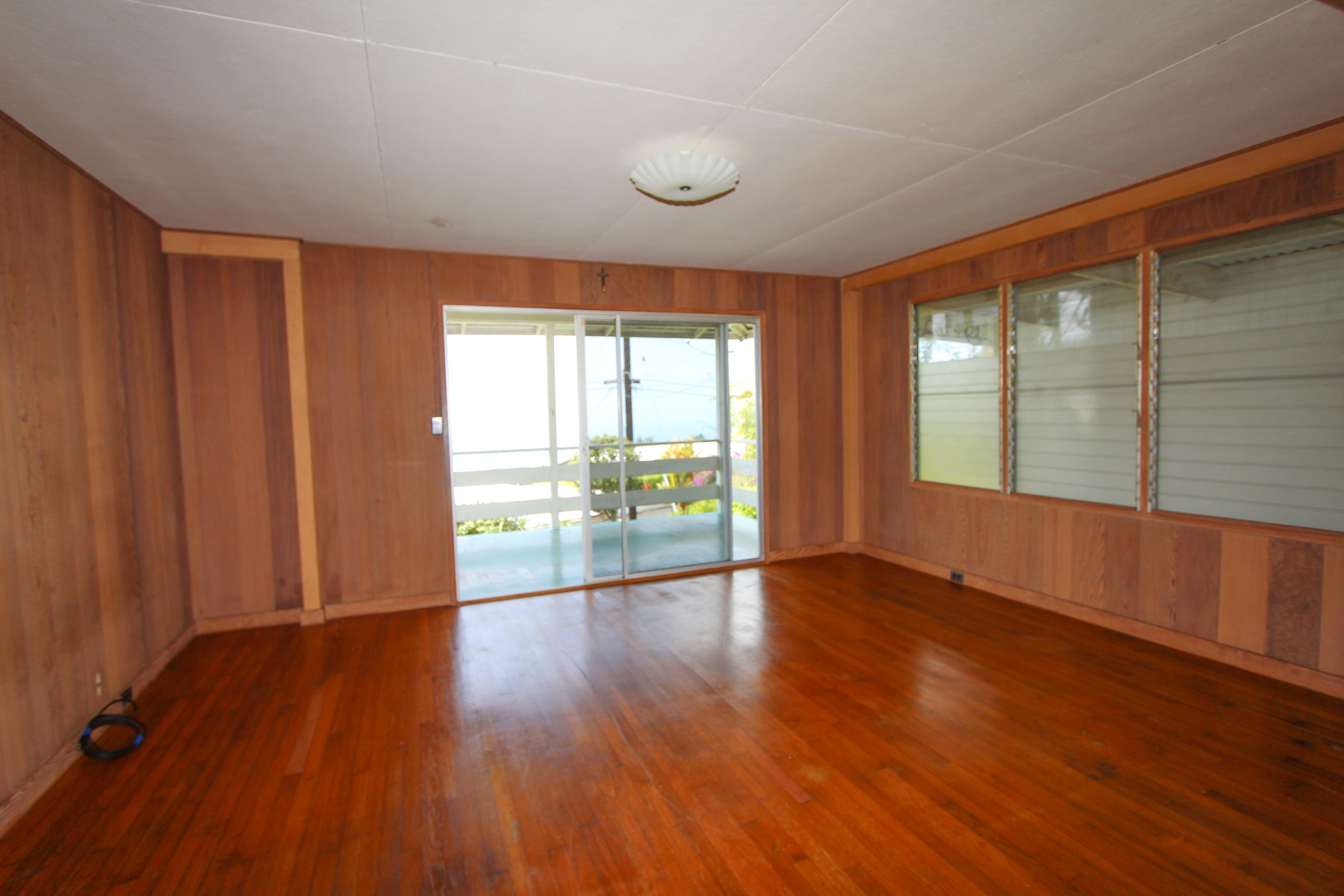 82-1025 Kinue Road Captain Cook, HI 96704 - Photo 5 of 12 an empty room with wooden floor and windows with curtains