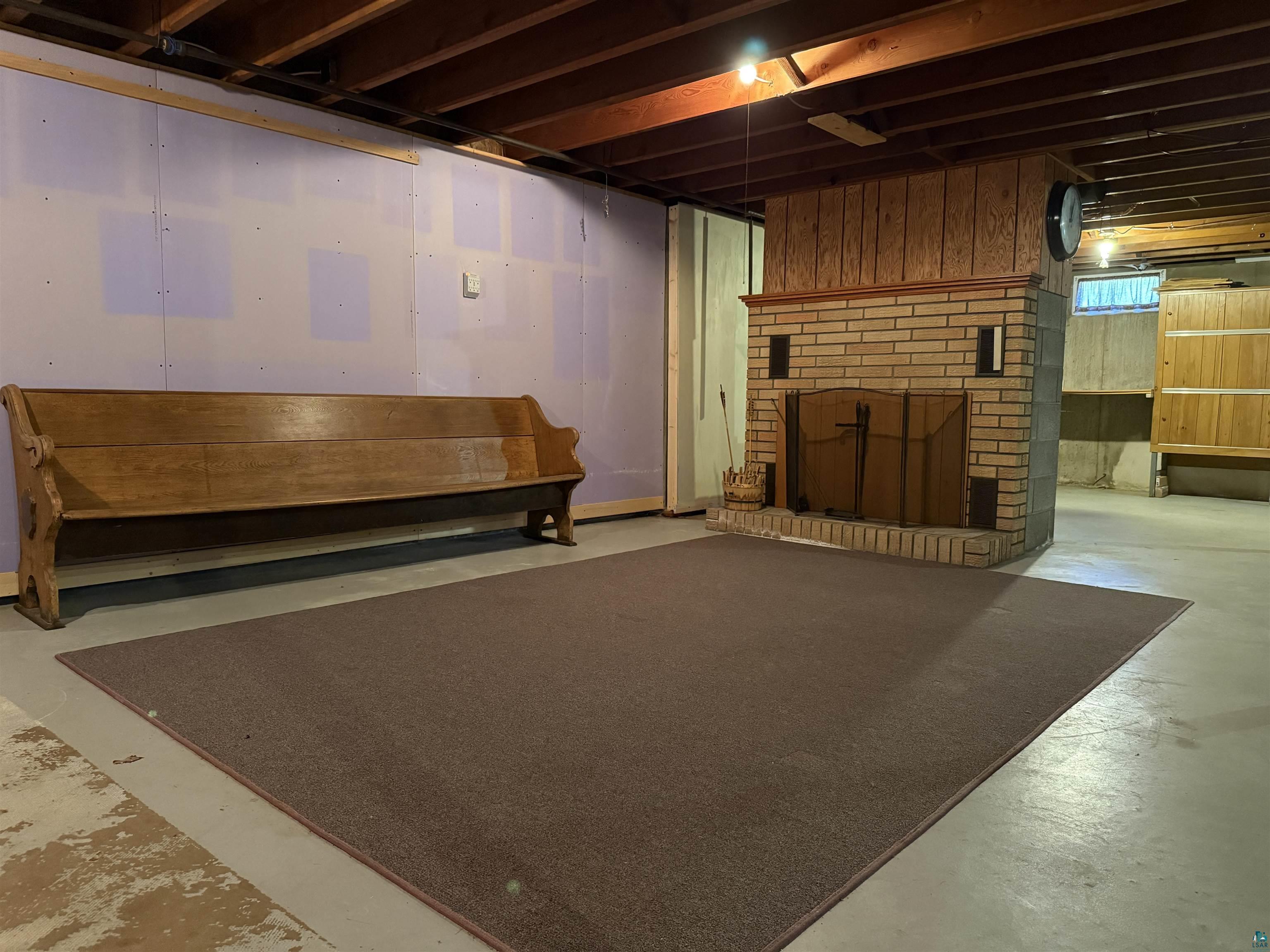 607 3rd Street Northeast Chisholm, MN 55719 - Photo 22 of 32 Finished lower level featuring an exposed wood beam ceiling, brick fireplace with metal screen, wood paneling, and concrete flooring