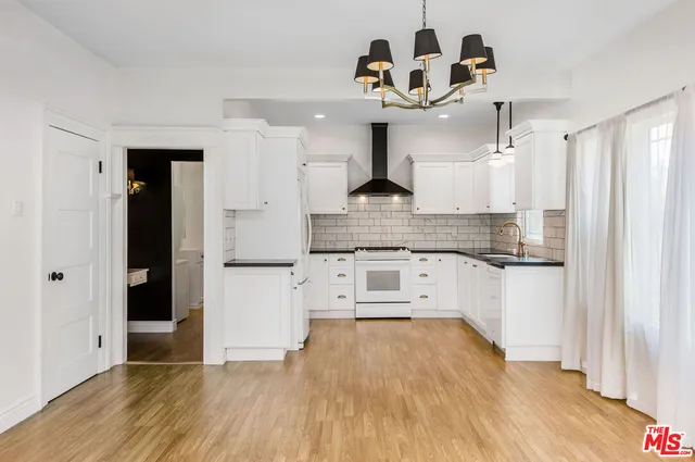 a kitchen with stainless steel appliances granite countertop a refrigerator a stove and white cabinets with wooden floor