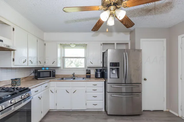 a kitchen with stainless steel appliances a refrigerator a sink and white cabinets