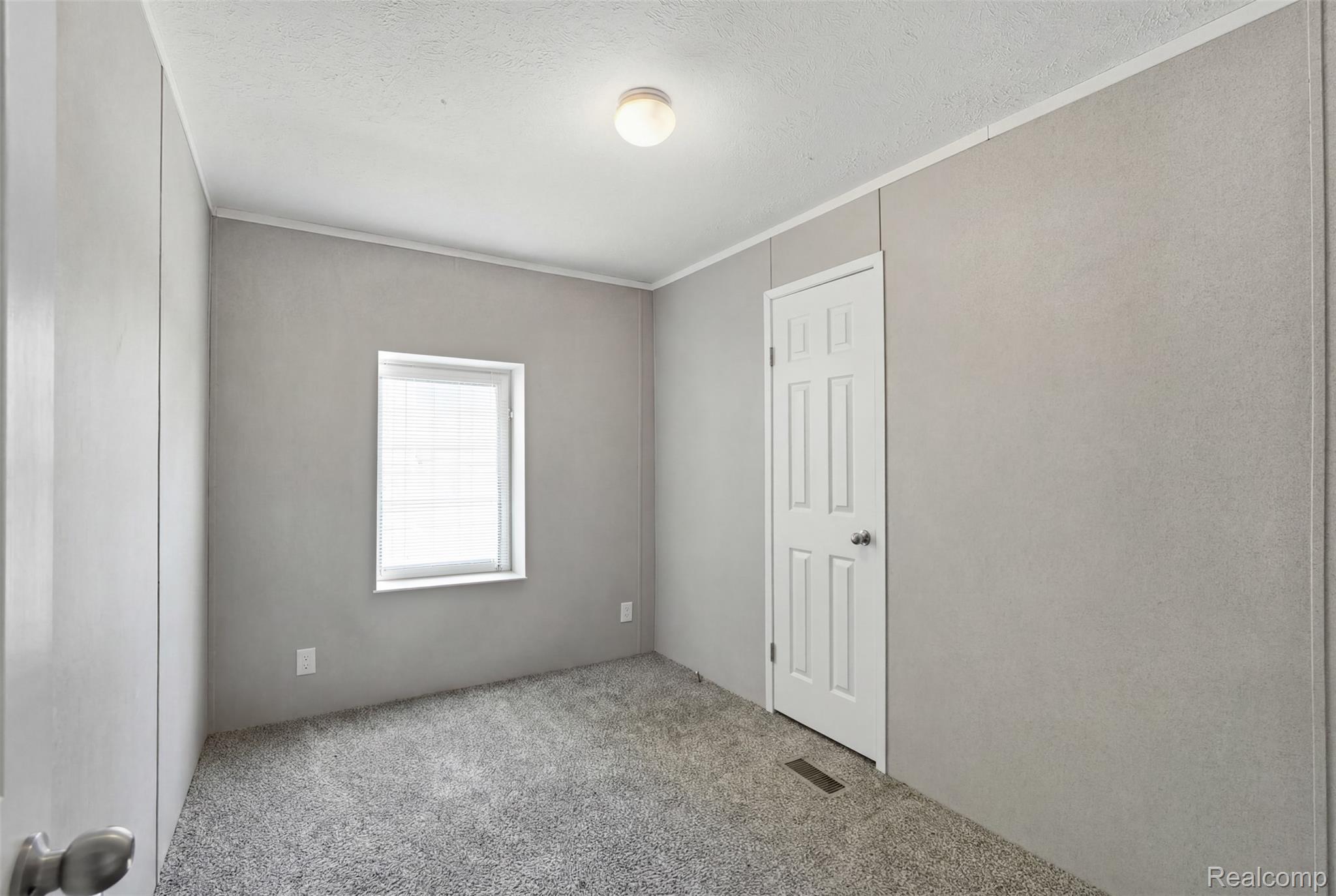 92 Normandy Drive Howell, MI 48843 - Photo 14 of 24 Neutral-toned room featuring light gray walls, plush gray carpet, a white paneled door, and a single window with blinds