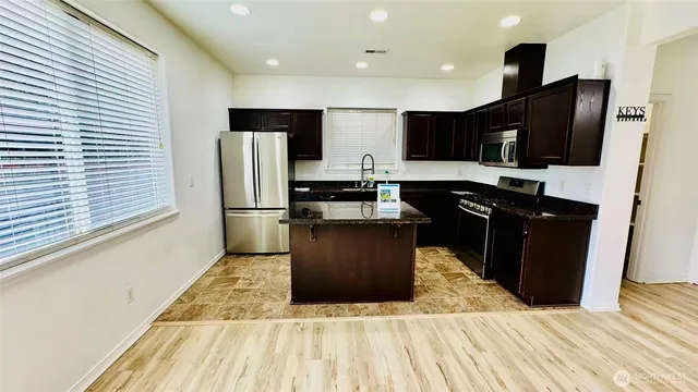 a kitchen with stainless steel appliances kitchen island granite countertop a refrigerator a stove top oven and a sink with wooden floor