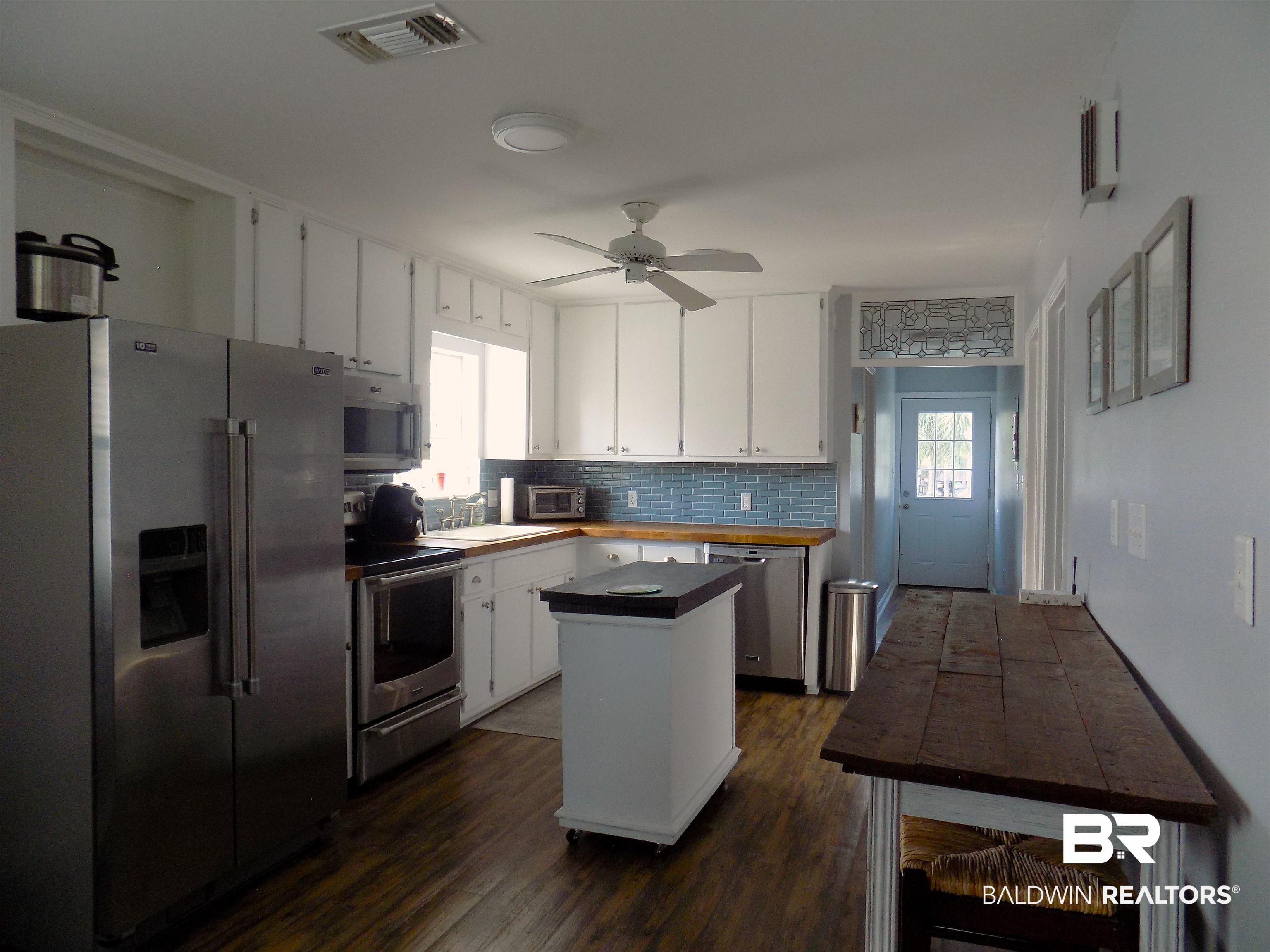304 Windmill Ridge Road Gulf Shores, AL 36542 - Photo 6 of 29 Kitchen featuring appliances with stainless steel finishes, decorative backsplash, white cabinetry, dark wood-style floors, and a center island