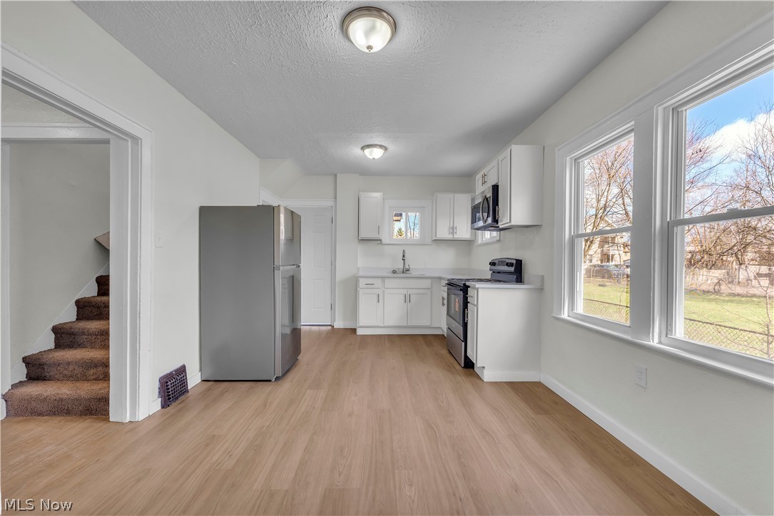 12905 Watterson Avenue Cleveland, OH 44105 - Photo 6 of 30 Kitchen with light countertops, stainless steel appliances, white cabinetry, a textured ceiling, and light wood finished floors