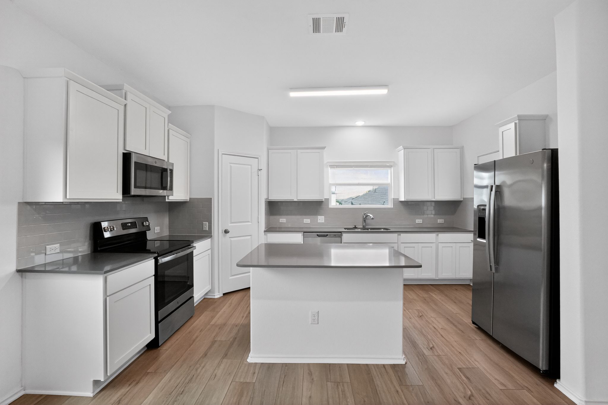 412 Perfect World Loop Jarrell, TX 76537 - Photo 6 of 15 Bright kitchen featuring wood-finish flooring, white cabinetry, dark countertops, a tile backsplash, and stainless steel appliances