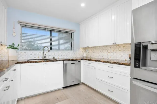 a kitchen with granite countertop white cabinets stainless steel appliances and a window